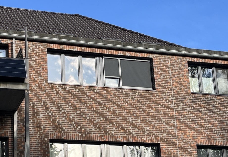 Klinkerfassade mit Sonnenschutzrollos von CLIP'N'SHADE an zwei Fenstern von außen.